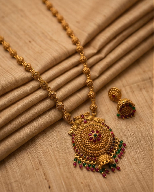 Gold necklace with intricate design and red and green gemstones on a beige fabric background