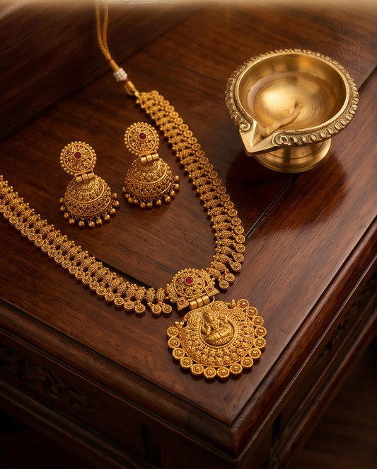 Gold necklace and earrings set on a wooden surface with a small brass lamp.