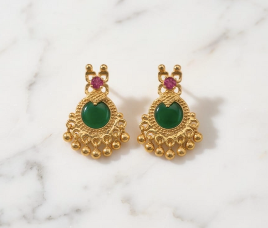 Gold earrings with green gemstones on a marble background