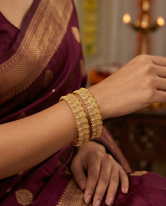 Gold bracelets on a person wearing a purple saree with a blurred background