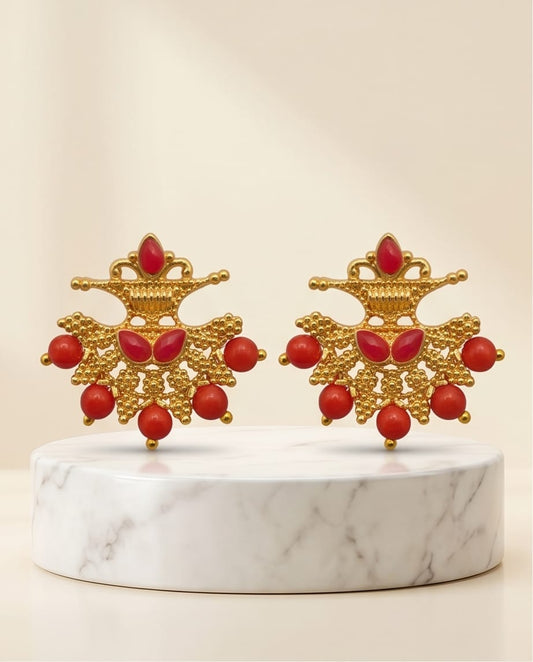 Pair of gold earrings with red beads on a marble stand against a beige background
