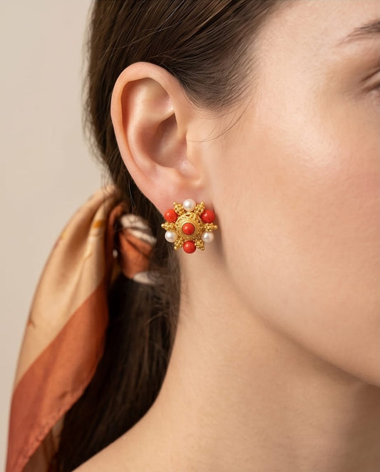 Close-up of a woman wearing gold earrings with red and white stones against a neutral background